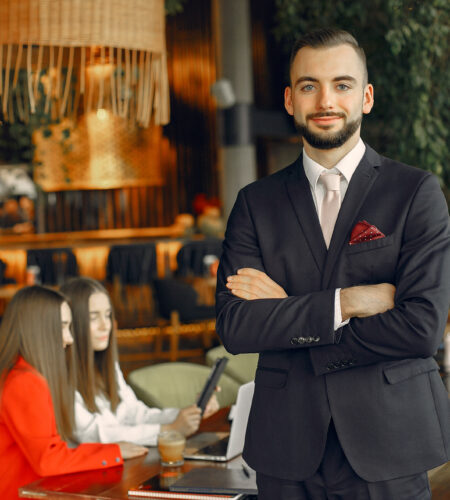 A man standing with folded hands wearing black suit in restaurant